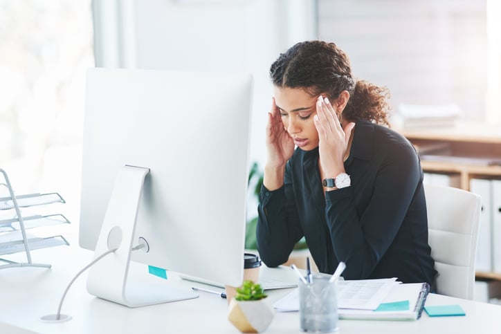 Stressed office employee sitting at a desk, holding her head while looking at a computer screen.