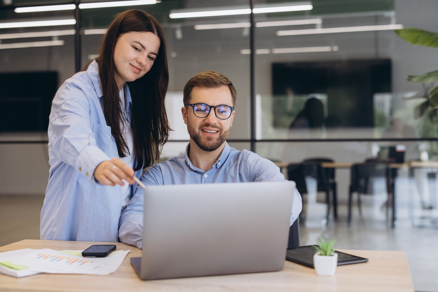 Colleague showing a coworker how to use software on a laptop in a modern office