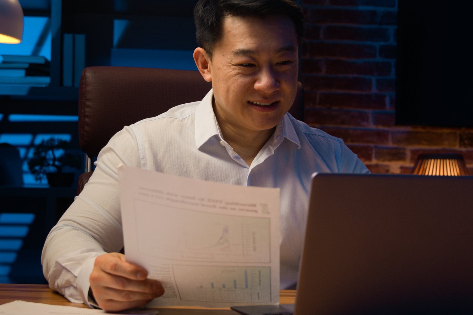 Business owner reviewing financial reports late at night beside a laptop
